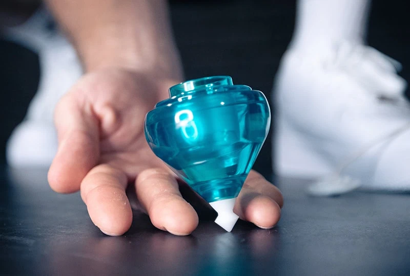 Hand scooping a spinning teal top off the floor