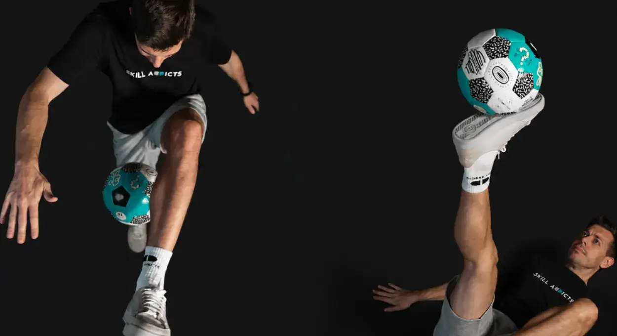 Two freestyle football players doing tricks with the teal ball